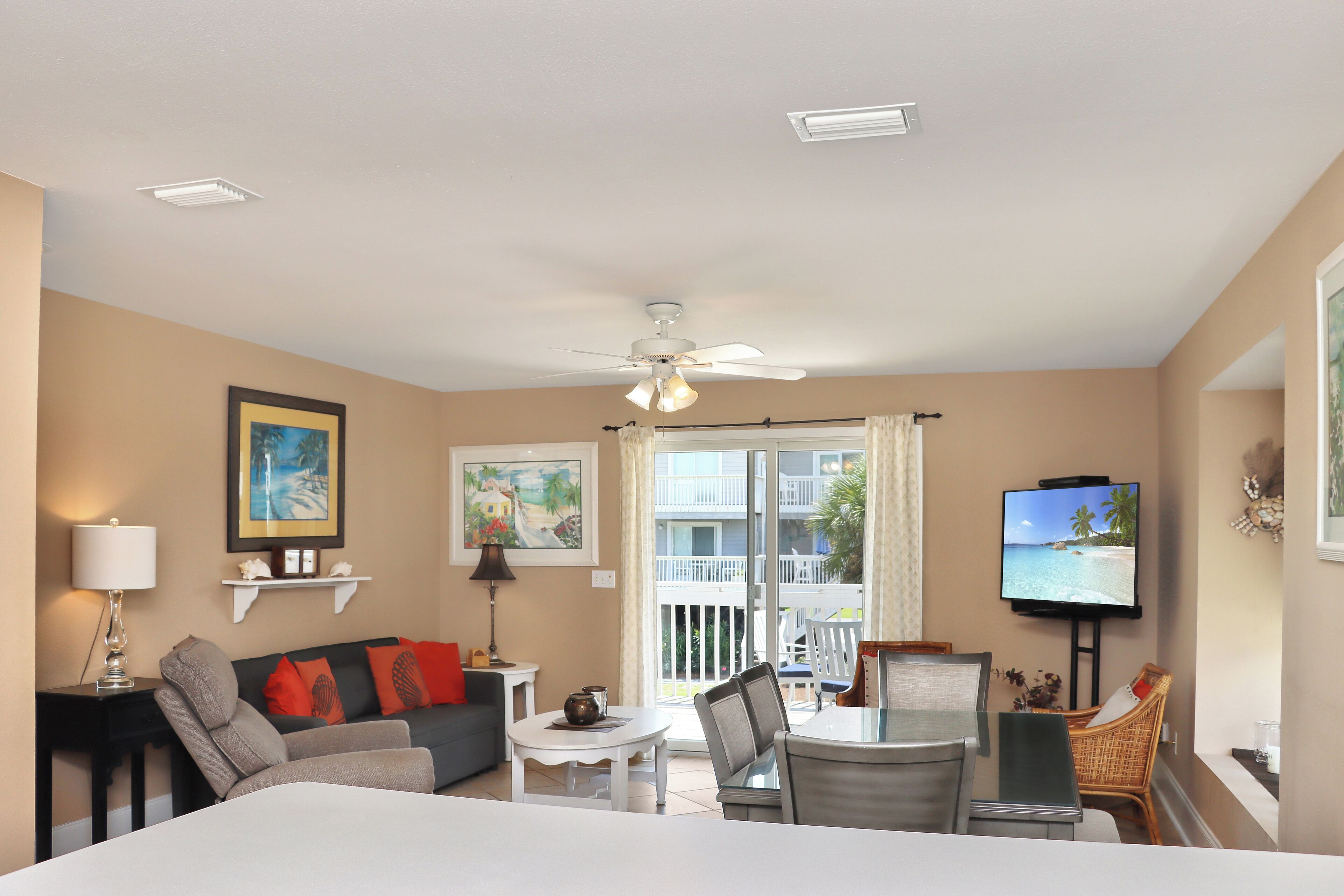 Una sala de estar con sofá, mesa de comedor, sillas, televisor y un balcón con vista a la playa.