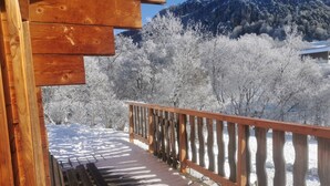 Une terrasse en bois dotée d’une rambarde, qui donne sur un paysage enneigé avec des arbres et des montagnes en arrière-plan.