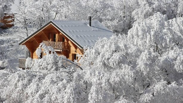 Une cabane en bois dotée d’un balcon, entourée d’arbres couverts de neige.
