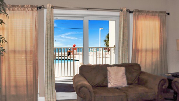 Ein Wohnzimmer mit einer Couch, Blick auf einen Pool und einem Balkon mit Geländer.