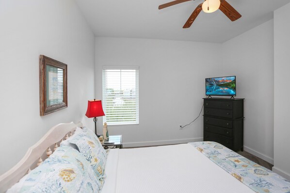 A bedroom with a bed, a television on a dresser, a window with blinds, a ceiling fan, and a framed picture on the wall. - Gulf View, Gated Community with Pool, WiFi ~ Waterside Village Condo 302 (Mexico Beach)