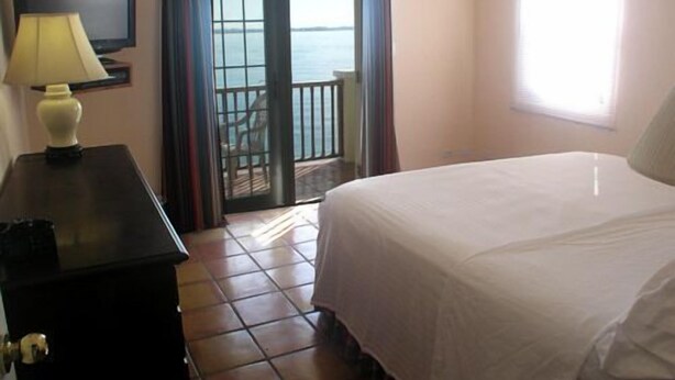 A hotel room with a bed, a desk with a lamp, a TV, and a balcony with a view of the sea. - Waterfront 2 Bedroom Cottage, Access to Private Beach (Somerset Village)