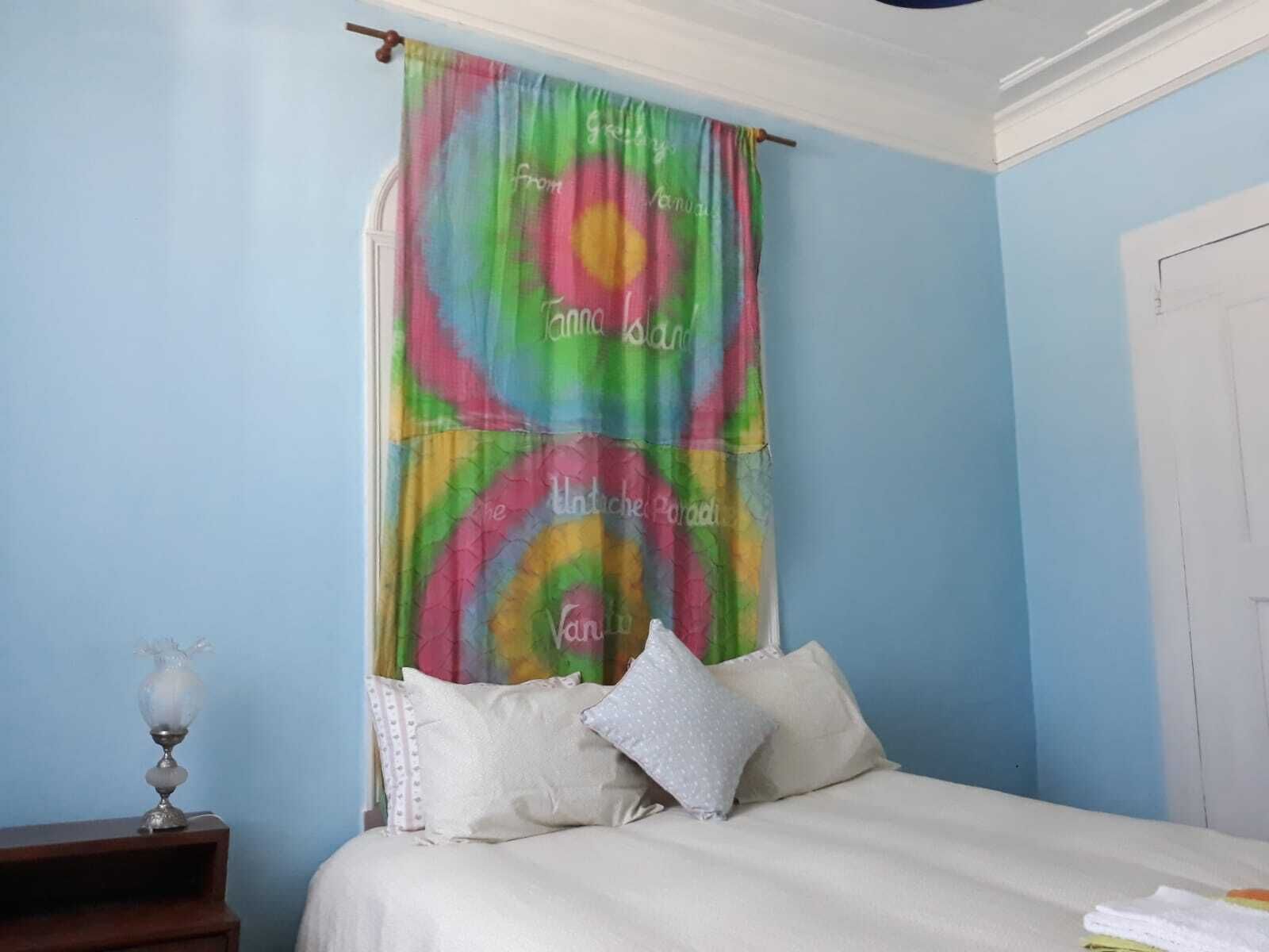 A bedroom with a bed, pillows, a nightstand, and a colorful curtain.