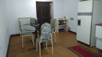 A small, compact room with a dining table and four chairs, a refrigerator, and a radiator.