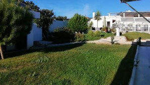 A well-maintained garden with a variety of plants and a white building with a glass greenhouse.