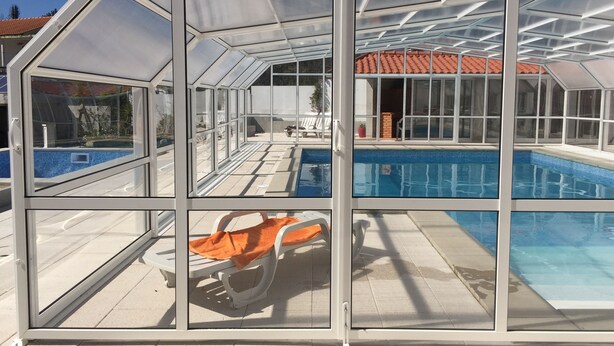 A glass-enclosed swimming pool with a tiled deck and a lounge chair.