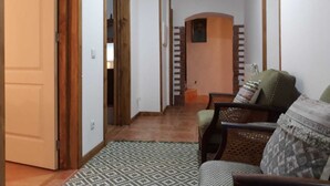 A hallway with a patterned rug, a wooden door, a staircase, and a seating area with a patterned cushion.