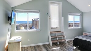 Une chambre avec vue sur l’océan, un téléviseur fixé au mur et un escalier menant à un balcon.