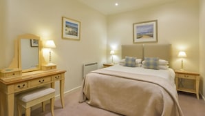 Une chambre à coucher comprenant un lit, des tables de chevet, une commode, un banc et deux tableaux encadrés accrochés aux murs.