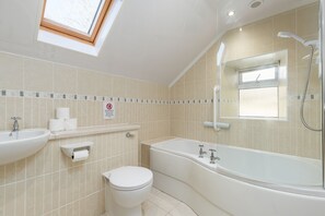 Une salle de bain avec un puits de lumière, une baignoire, des toilettes et un lavabo.