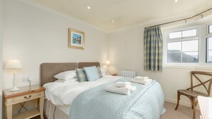 A bedroom with a large bed, two bedside tables, a chair, a window with curtains, and a wall-mounted picture. - Quarry Cottage -  a detatched single storey cottage sleeping up to 6 (Oban)