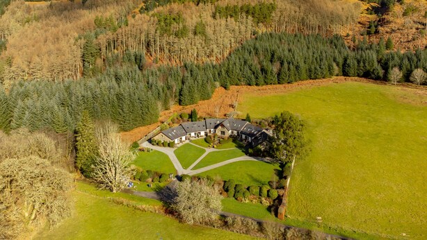 Vista aérea de un complejo arquitectónico grande y circular rodeado de un césped cuidado y un bosque denso.