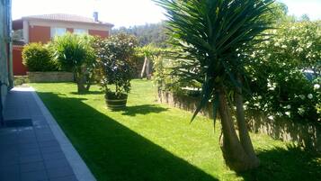 Un jardín bien cuidado con diversas plantas, césped y una casa al fondo.