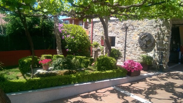 A stone building with a clock, surrounded by well-maintained hedges and flowering plants. - "EIRA VELLA" Holiday house, (from € 30 day / month). (Pontevedra)