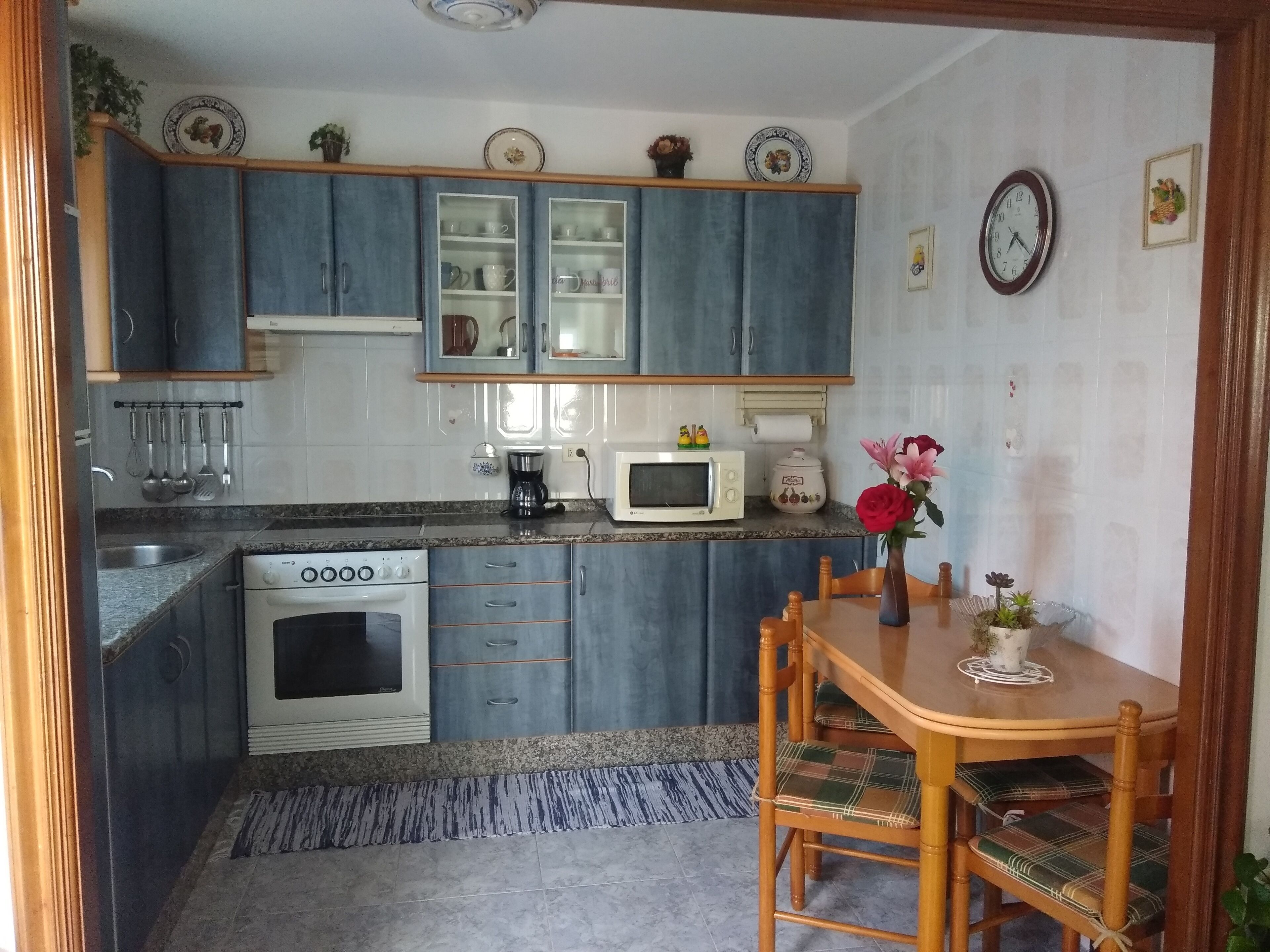 Une cuisine avec des meubles de rangement bleus, une cuisinière, un four à micro-ondes et une table à manger avec des chaises.