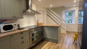 Een moderne keuken met grijze kastjes, een roestvrijstalen afzuigkap, een magnetron en een houten aanrecht.