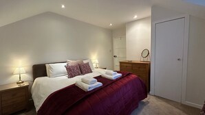 Een slaapkamer met een bed, nachtkastjes, een dressoir, een spiegel en een deur.