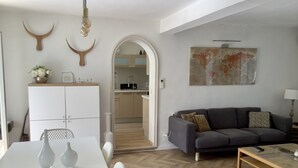 A modern living room with a grey sofa, a coffee table, and a dining table with two vases. There is a kitchen visible through an archway, and a map artwork on the wall. - PRETTY PROVENCAL VILLA WITH POOL (Le Tignet)