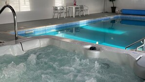 En inomhuspool med bubbelbad, träbjälkar och en sittgrupp med stolar.