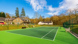 A tennis court with a net, surrounded by a green fence, and adjacent to a building with a stone facade.