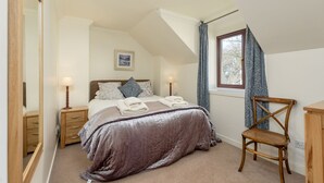 A bedroom with a bed, bedside tables, a chair, a window with curtains, and a ceiling light.