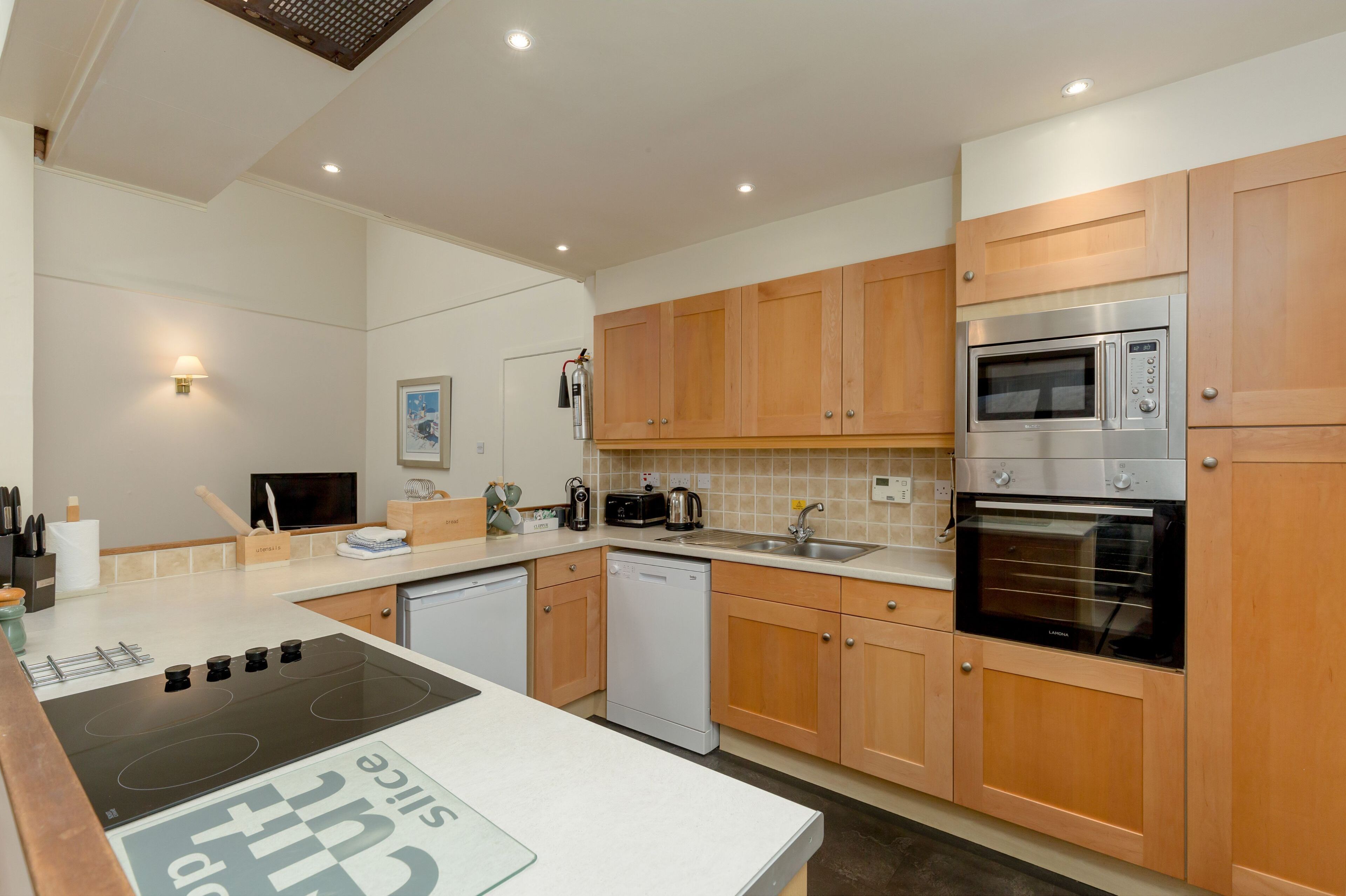 Een moderne keuken met houten kastjes, een ingebouwde magnetron, een vaatwasser en een fornuis.