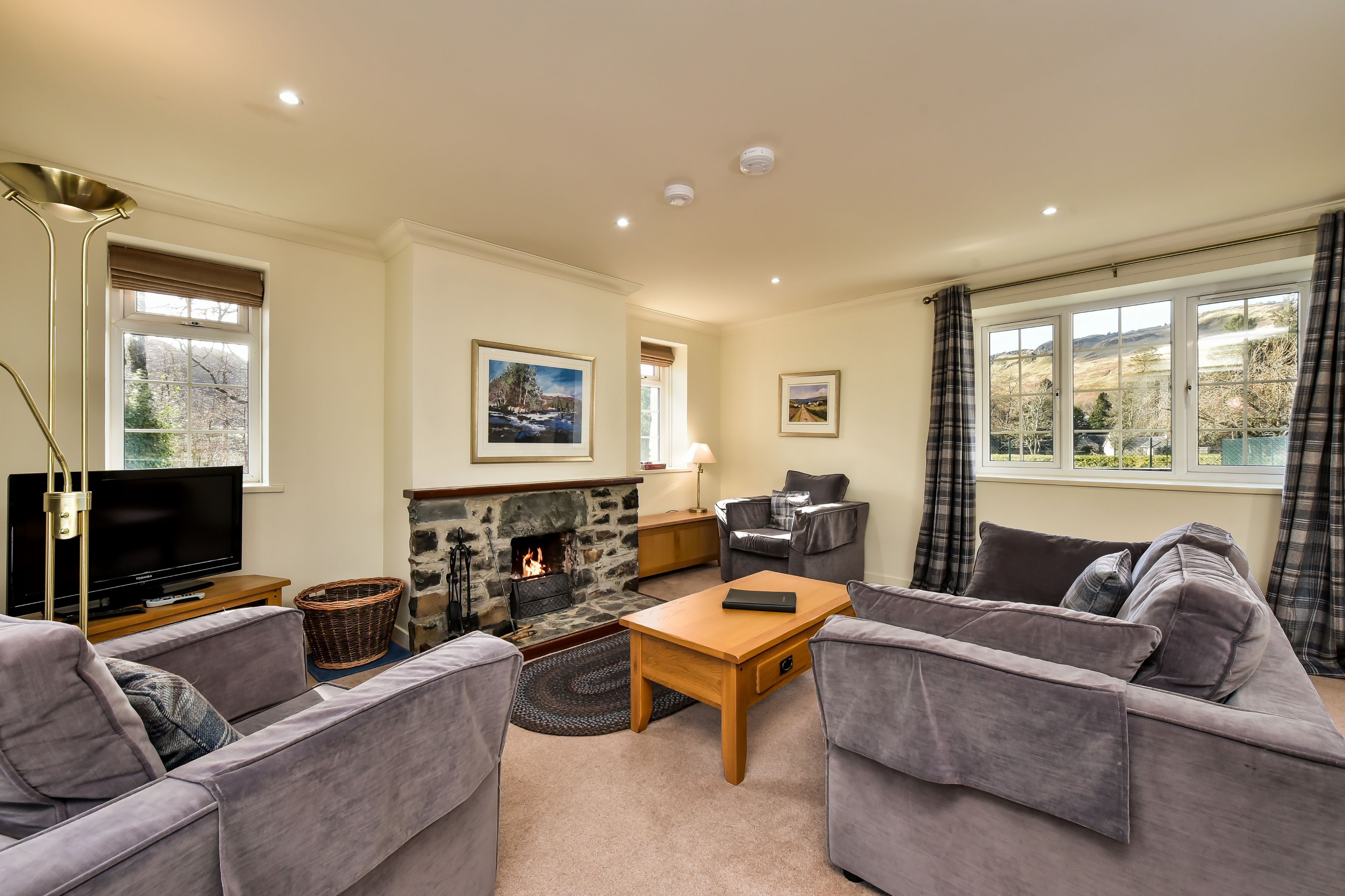 A living room with a fireplace, grey sofas, a television, and a stone wall.