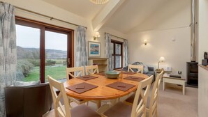 A dining area with a wooden table and chairs, a view of the outdoors, a sofa, a lamp, and a fireplace.