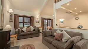 A spacious living room with two sofas, a wooden table, and a large window with curtains.