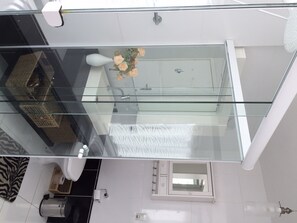 A modern bathroom with a glass-enclosed shower, a white toilet, a small sink, and a mirror.