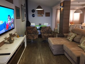 A living room with a television, two leopard print chairs, a sofa, a dining table with chairs, and a chandelier.