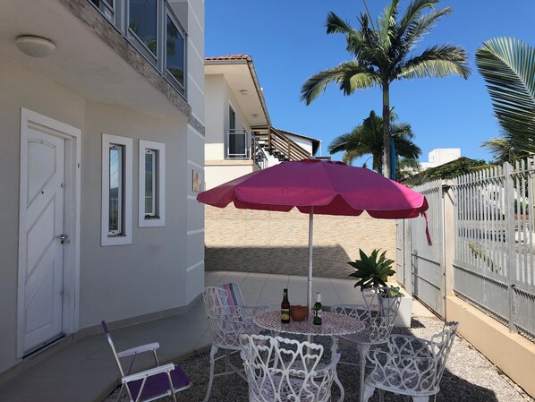 A patio with a table and chairs, a red umbrella, and a palm tree.