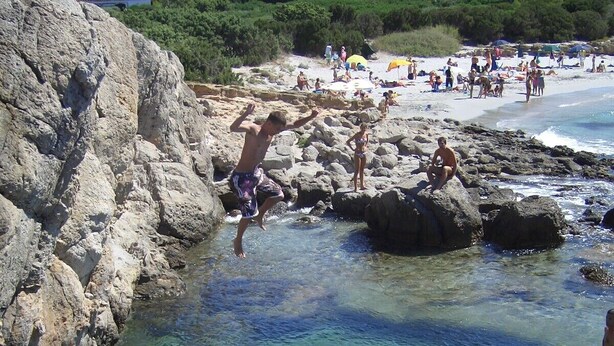 A rocky beach with clear water, a house in the background, and people enjoying the beach. - Spacious luxury villa with private swimming pool (Villaperuccio)