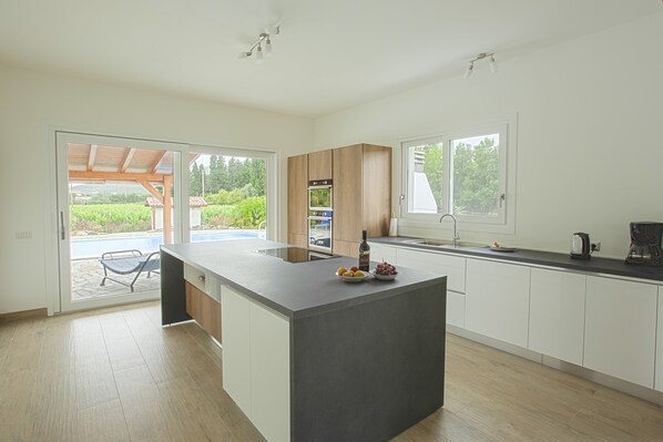 A modern kitchen with a central island, built-in appliances, and large windows offering views of greenery.