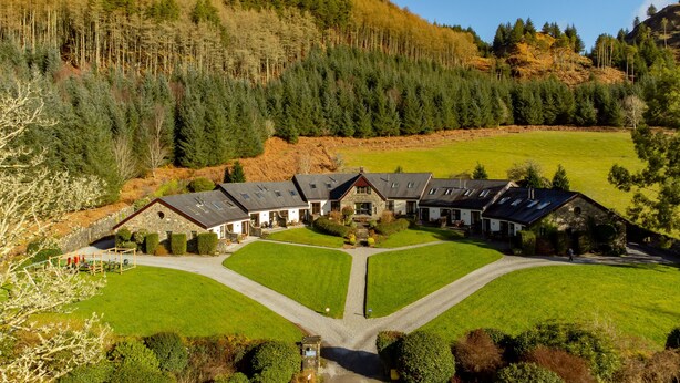 A large, multi-story building with a symmetrical layout, surrounded by well-maintained lawns and a forested hillside.