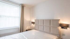 Ein ordentlich bezogenes Bett mit gepolstertem Kopfteil, einem Nachttisch und einer Wandleuchte.