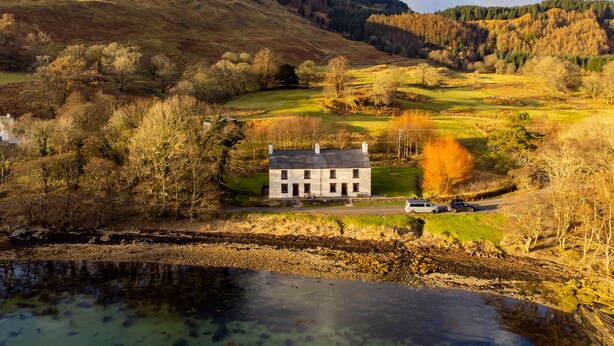 A stone house with a sloped roof, surrounded by a grassy area and a body of water. - Pier House 1 - Semi-detached, stone-built cottage on lochside (Oban)