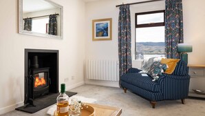 A living room with a fireplace, a sofa, a table with a bottle and glass, and a window with curtains. - Pier House 1 - Semi-detached, stone-built cottage on lochside (Oban)