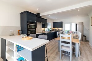 A modern kitchen with dark cabinetry, a central island, and a dining area with a wooden table and chairs.
