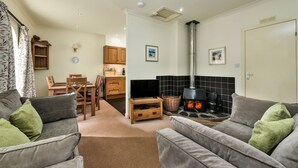 A living room with a fireplace, grey sofas, a television, and a dining area with wooden furniture. - Stables East -  a semi-detached cottage that sleeps up to 6 guests (Oban)