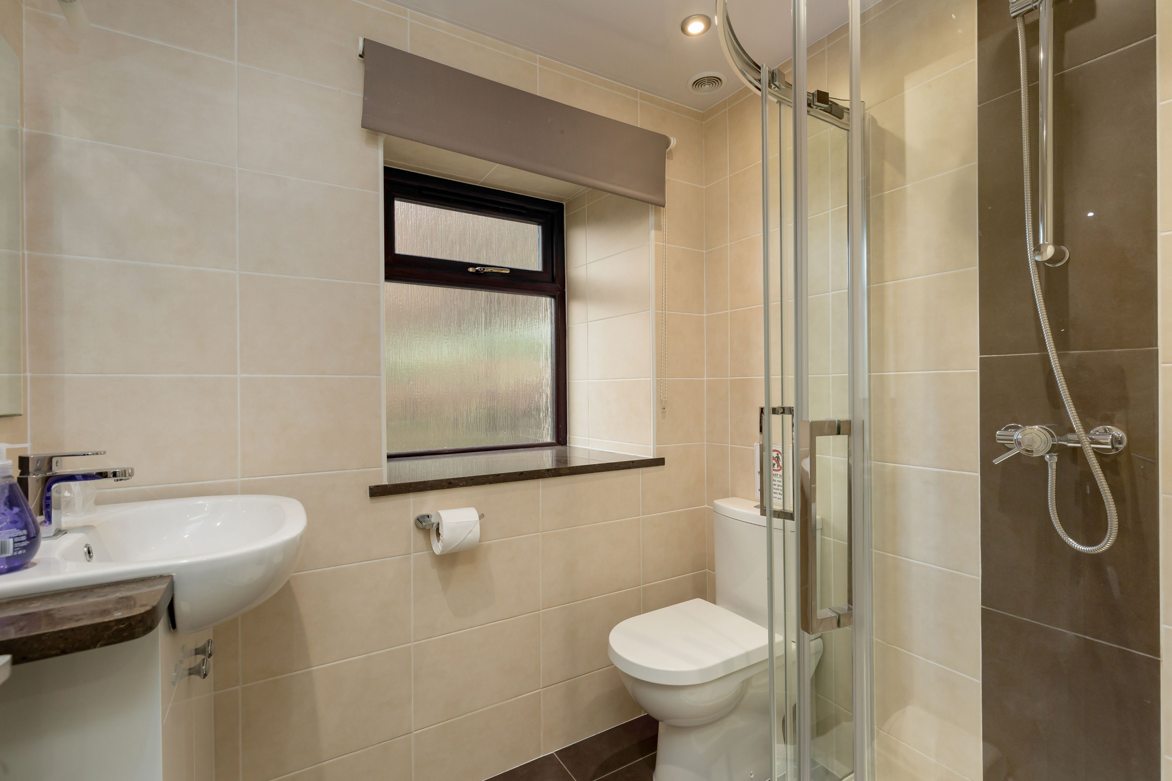 Un baño con ducha envuelta en vidrio, un lavabo blanco y un inodoro.