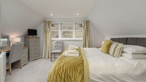 Un dormitorio con cama, escritorio, silla, televisor y ventana con cortinas.