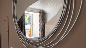 A round mirror reflecting a room with a window, curtains, and a small table with a candle.