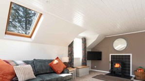 A living room with a sofa, a fireplace, a television, and a skylight.