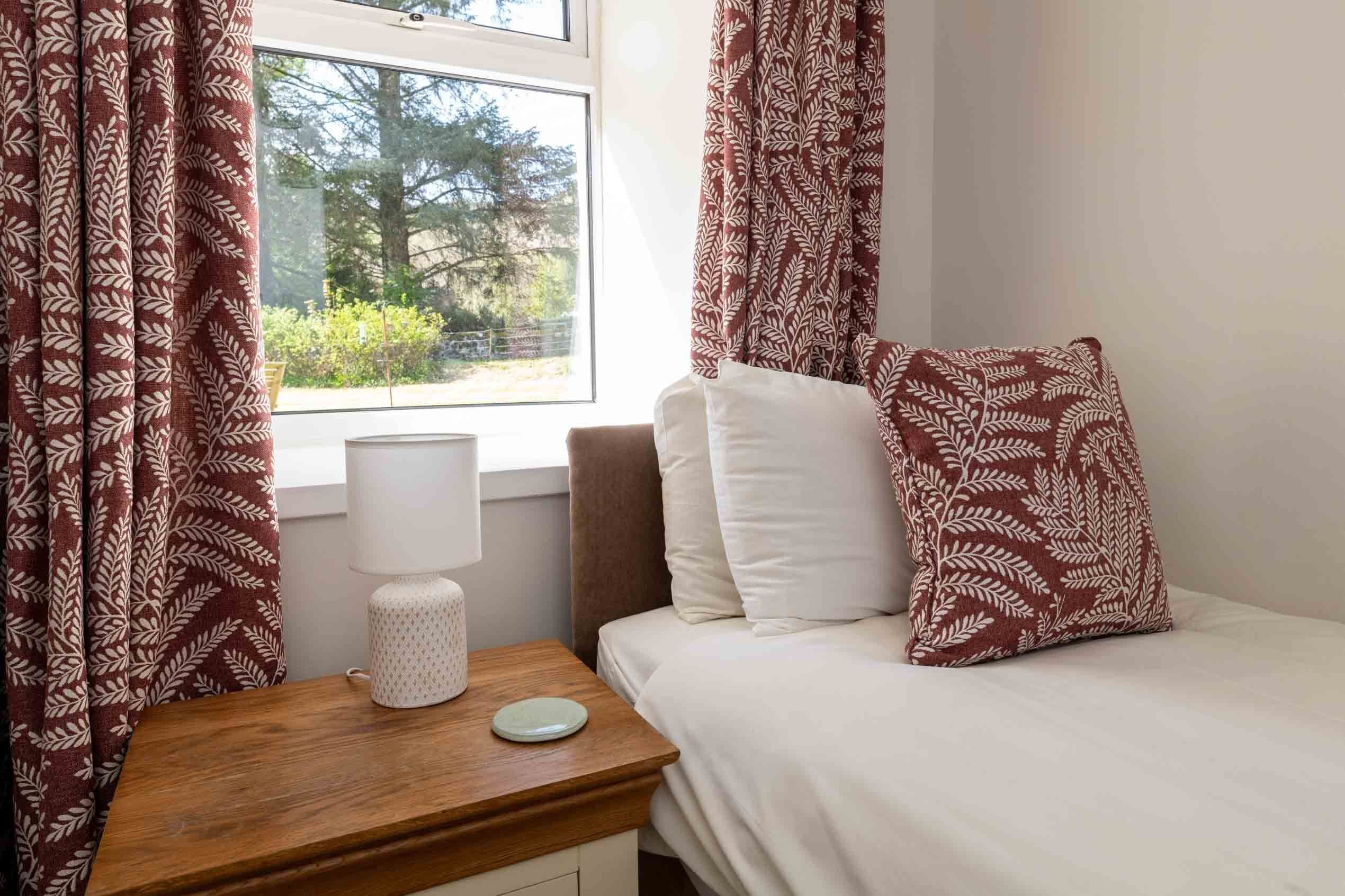 Un dormitorio con cama, mesita de noche, lámpara y cortinas.