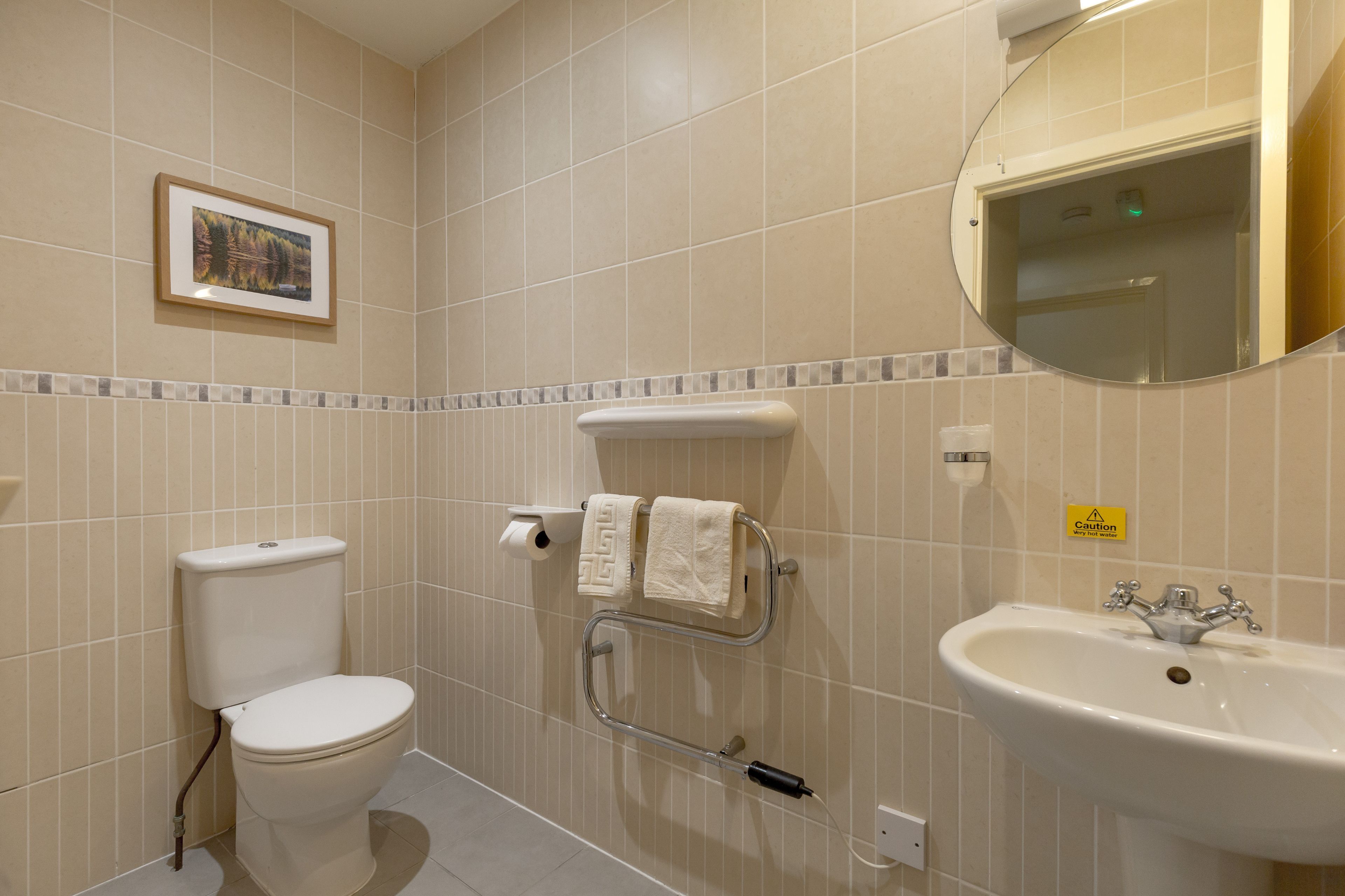 A bathroom with a toilet, a sink, a towel rack, and a framed picture on the wall.