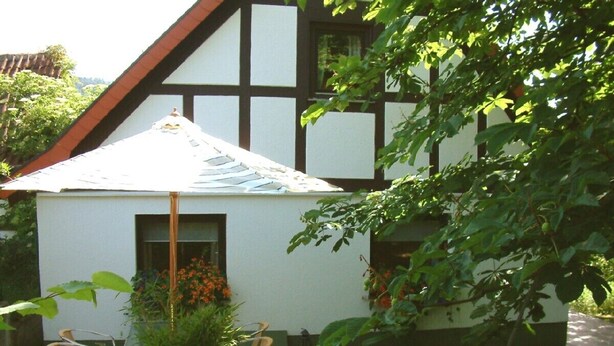 Une maison traditionnelle à colombages, dotée d’une terrasse en bois et de deux chaises.