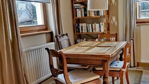 Un coin repas avec une table en bois, des chaises, une bibliothèque et une fenêtre avec des rideaux.