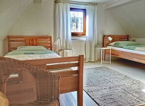 Une chambre confortable avec deux lits en bois, une petite table, une chaise en osier et une fenêtre avec des rideaux.
