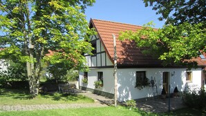 Une maison traditionnelle à colombages, avec un toit recouvert de tuiles rouges, entourée d’une pelouse bien entretenue et d’arbres.